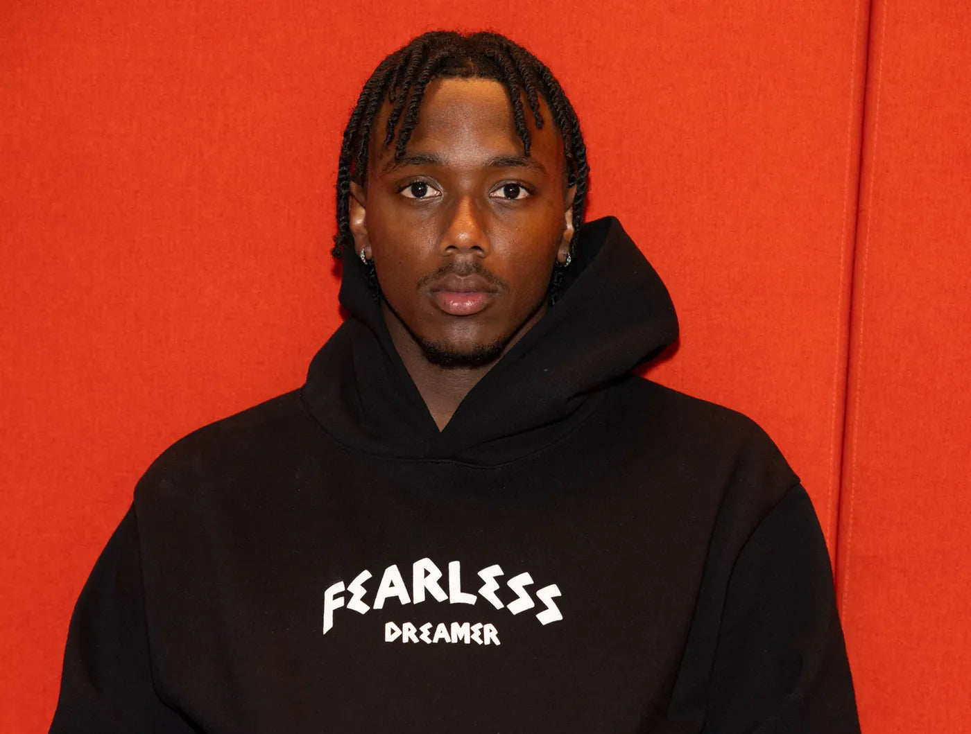 Model in a black Fearless Dreamer hoodie against an orange backdrop