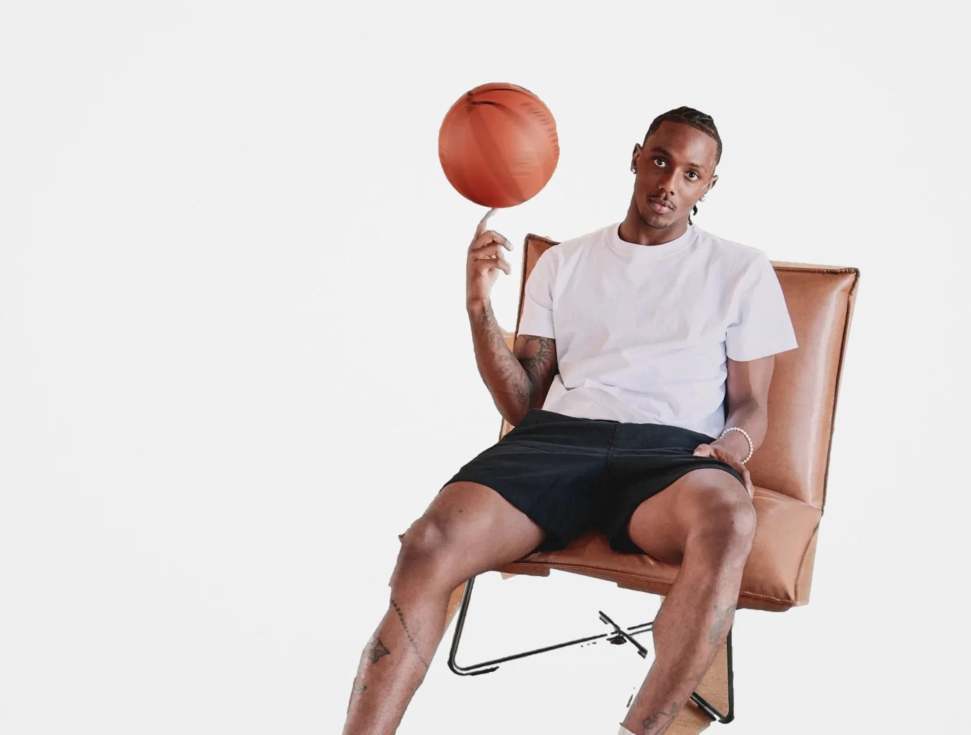 Model in a white tee and black shorts spinning a basketball while seated in a leather chair